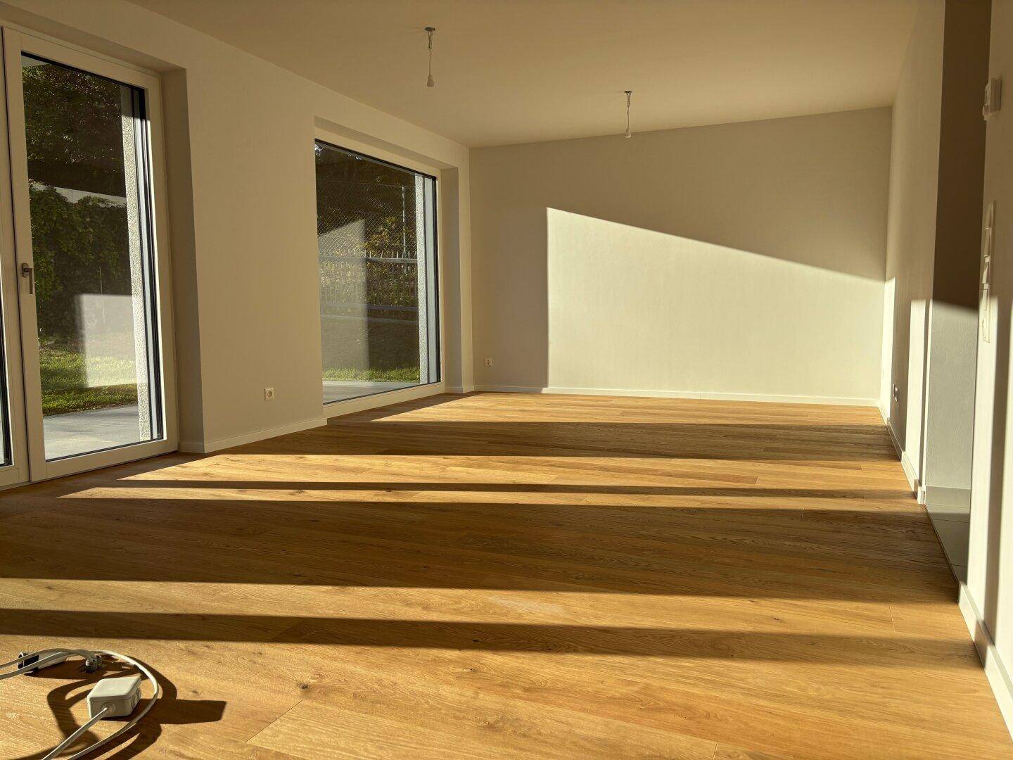 Geräumiger Wohnbereich mit hellem Parkettboden und viel natürlichem Licht durch große Fenster.