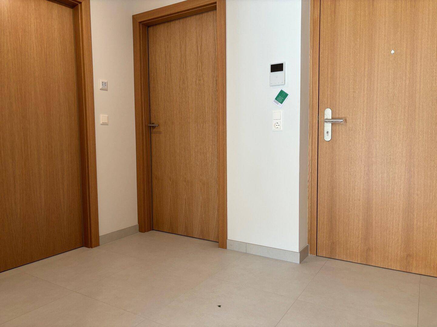 Heller Flur mit mehreren Holztüren und modernem Fliesenboden, der zu den Zimmern führt.