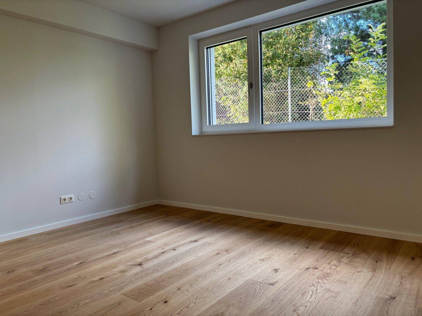 Helles Schlafzimmer mit neuem Parkettboden und Fenster mit Blick ins Grüne.