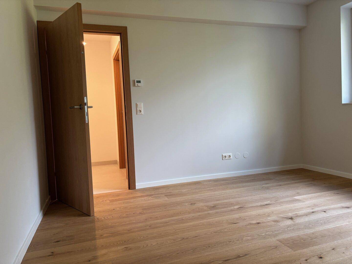 Geräumiges Schlafzimmer mit hellem Parkettboden und Zugang zu weiteren Räumen.