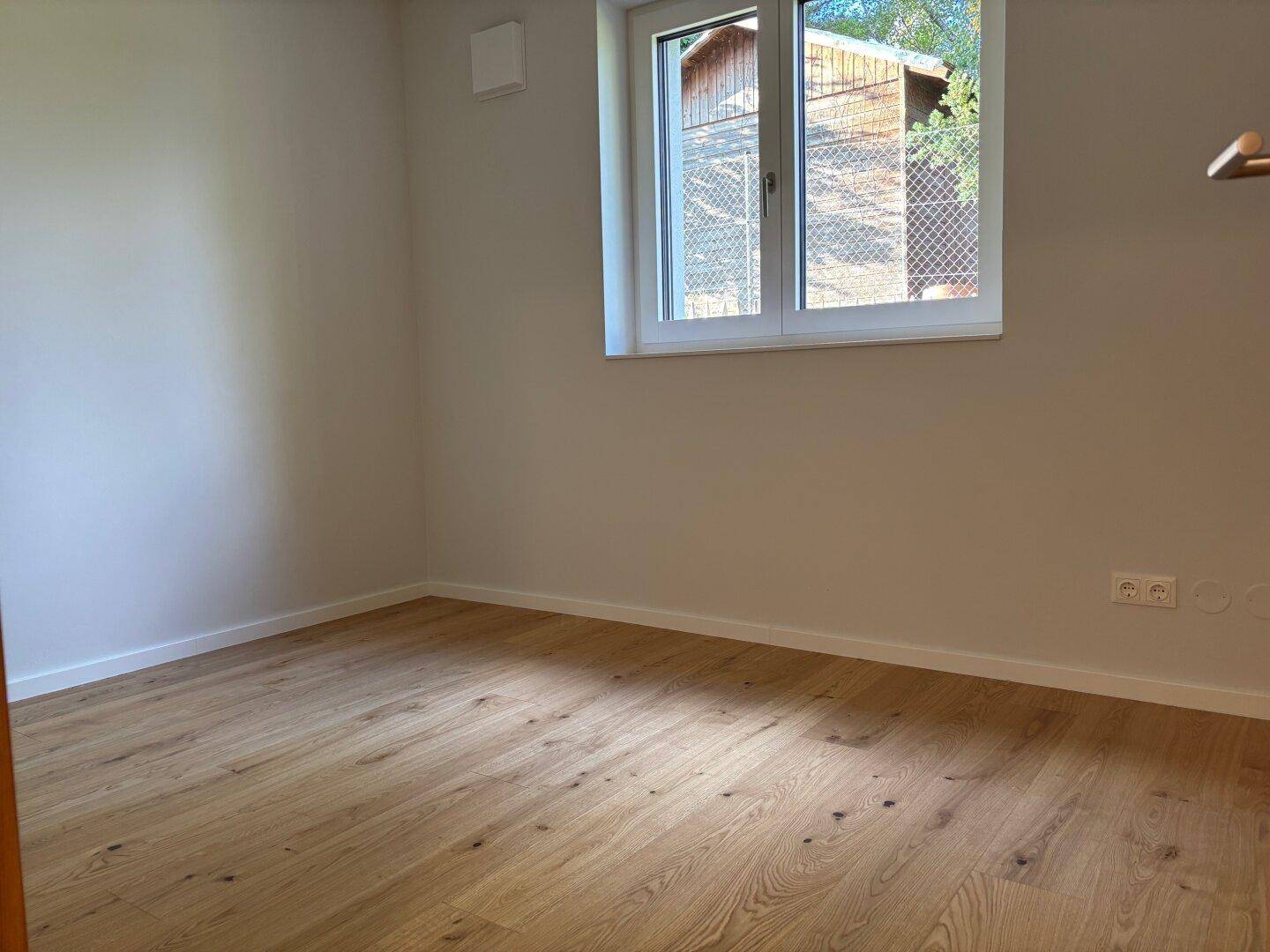 Ruhiges Schlafzimmer mit Parkettboden und Fenster, das viel Tageslicht hereinlässt.