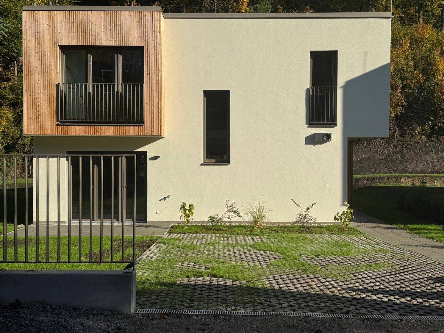 Vorderansicht eines modernen Hauses mit Holzverkleidung, großen Fenstern und französischen Balkonen.