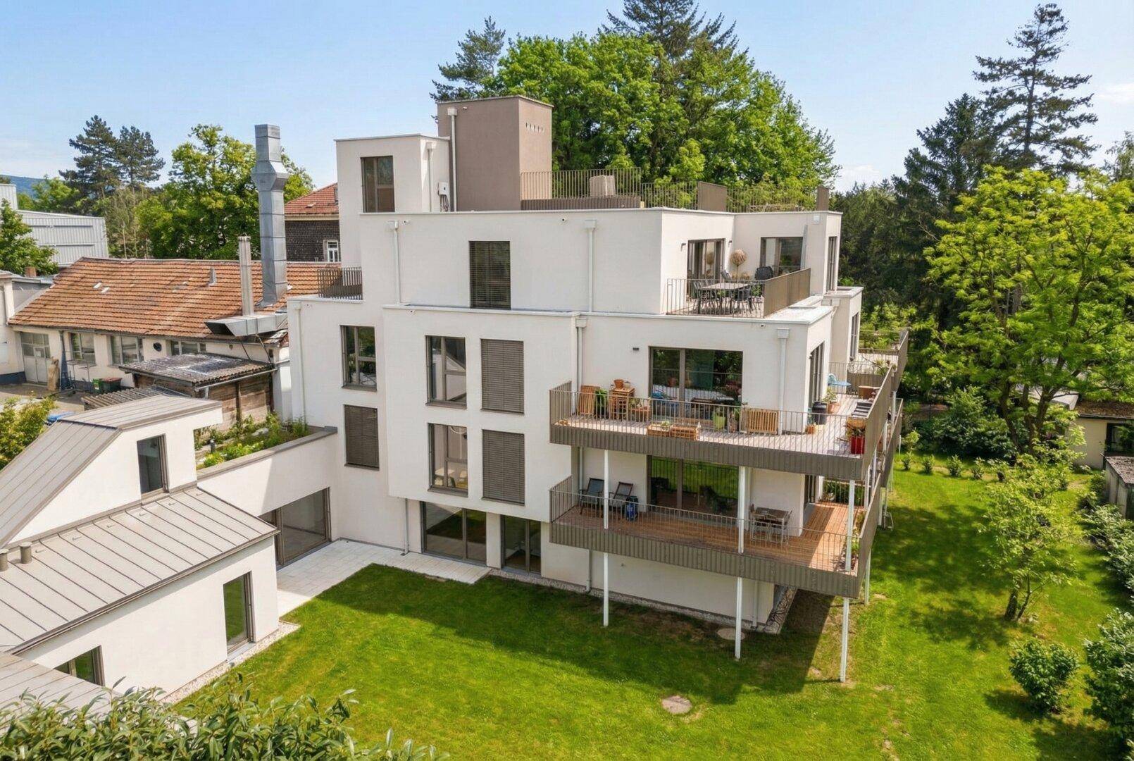 Moderner Neubau mit Terrassen und Balkonen, eingebettet in eine grüne Umgebung.