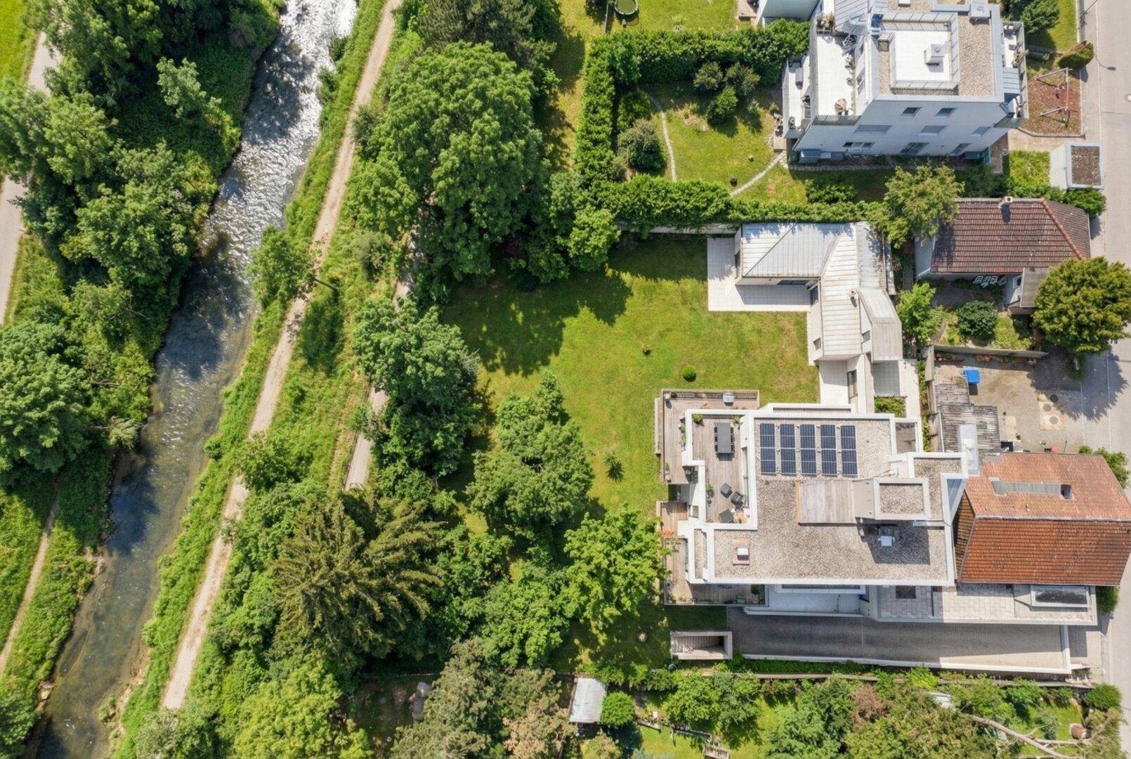 Luftaufnahme des Grundstücks mit modernem Gebäude, Photovoltaikanlage und angrenzendem Bachlauf.