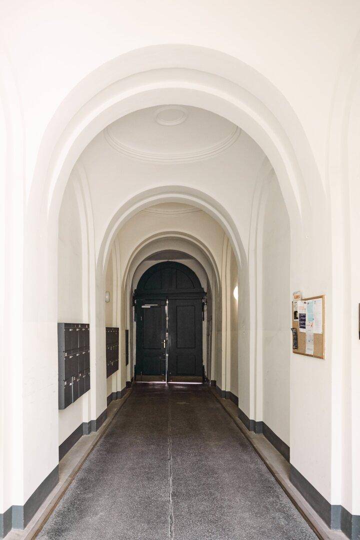 Langer, gewölbter Flur im Erdgeschoss eines Altbaus mit dunkler Eingangstür und Briefkästen.