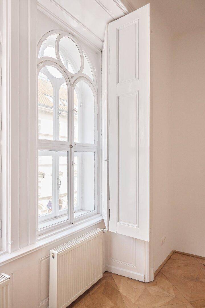 Detailansicht eines kunstvollen Bogenfensters mit geöffnetem Fensterladen und Heizkörper, in einem Altbauzimmer.