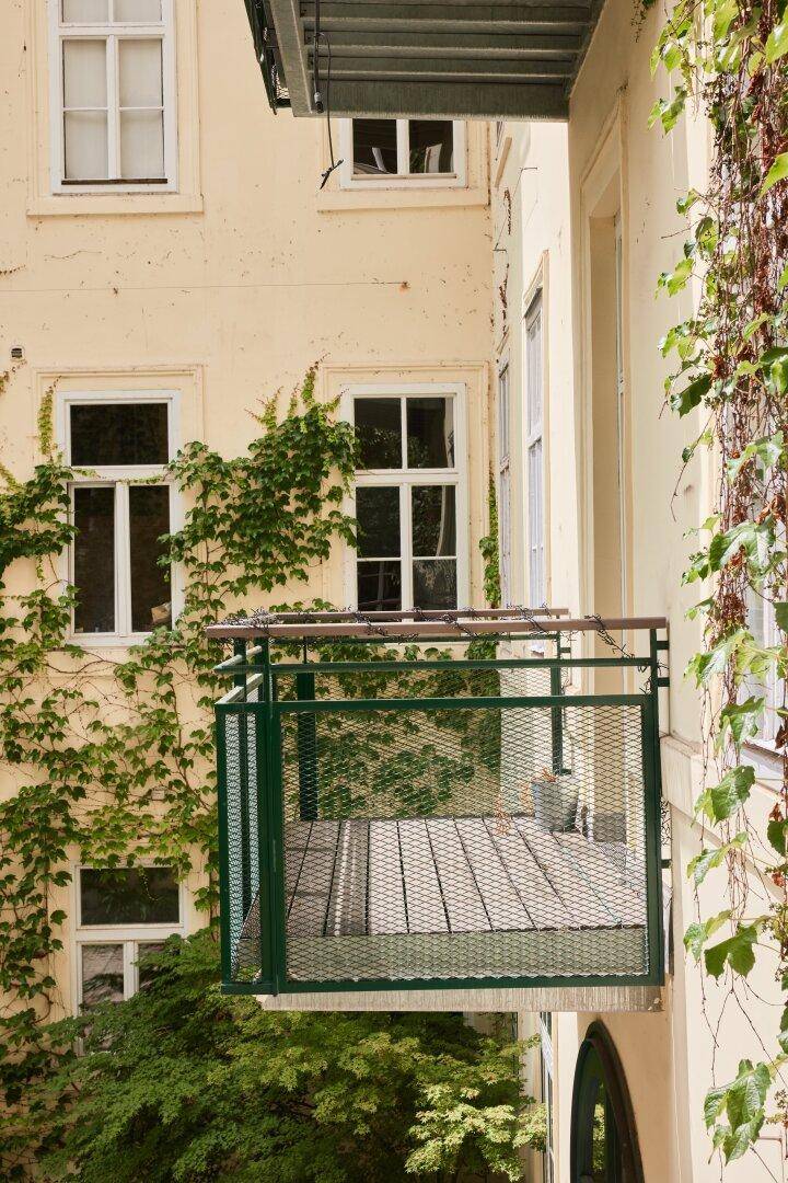 Kleiner grüner Metallbalkon an einer mit Efeu bewachsenen Fassade eines Altbaus, mit Blick in den Hof.