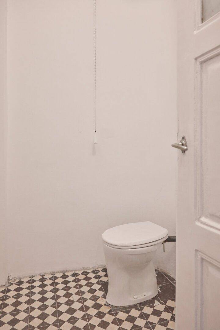 Einfaches WC mit Toilette und auffälligem schwarz-weiß kariertem Fliesenboden.
