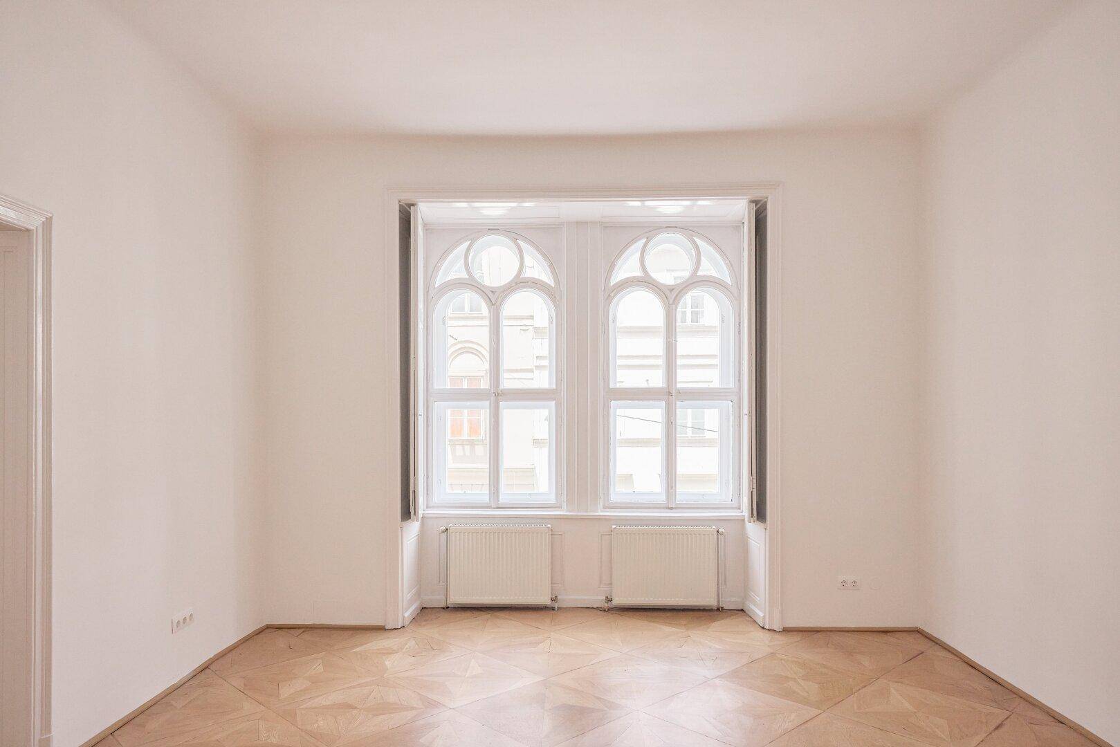 Geräumiges Zimmer mit eleganten Bogenfenstern, Parkettboden und geschlossenen Fensterläden, in einem Altbau.