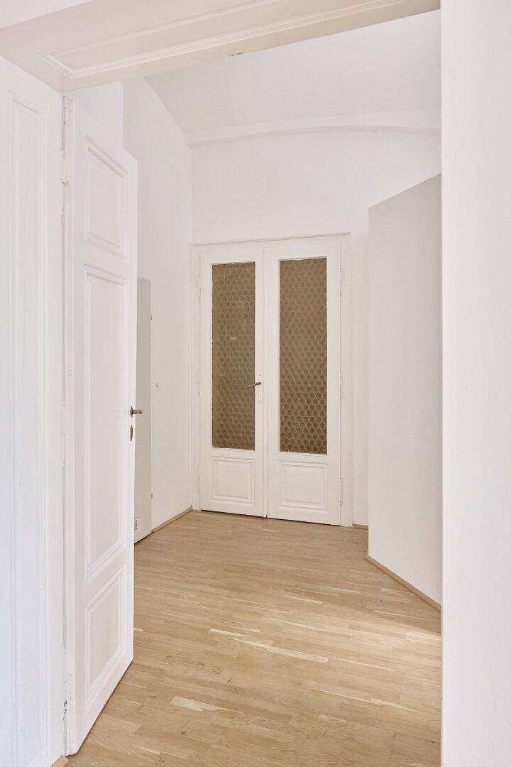 Blick durch eine offene Tür in einen weiteren Raum mit Holzdielenboden und einer Doppeltür mit Glas.