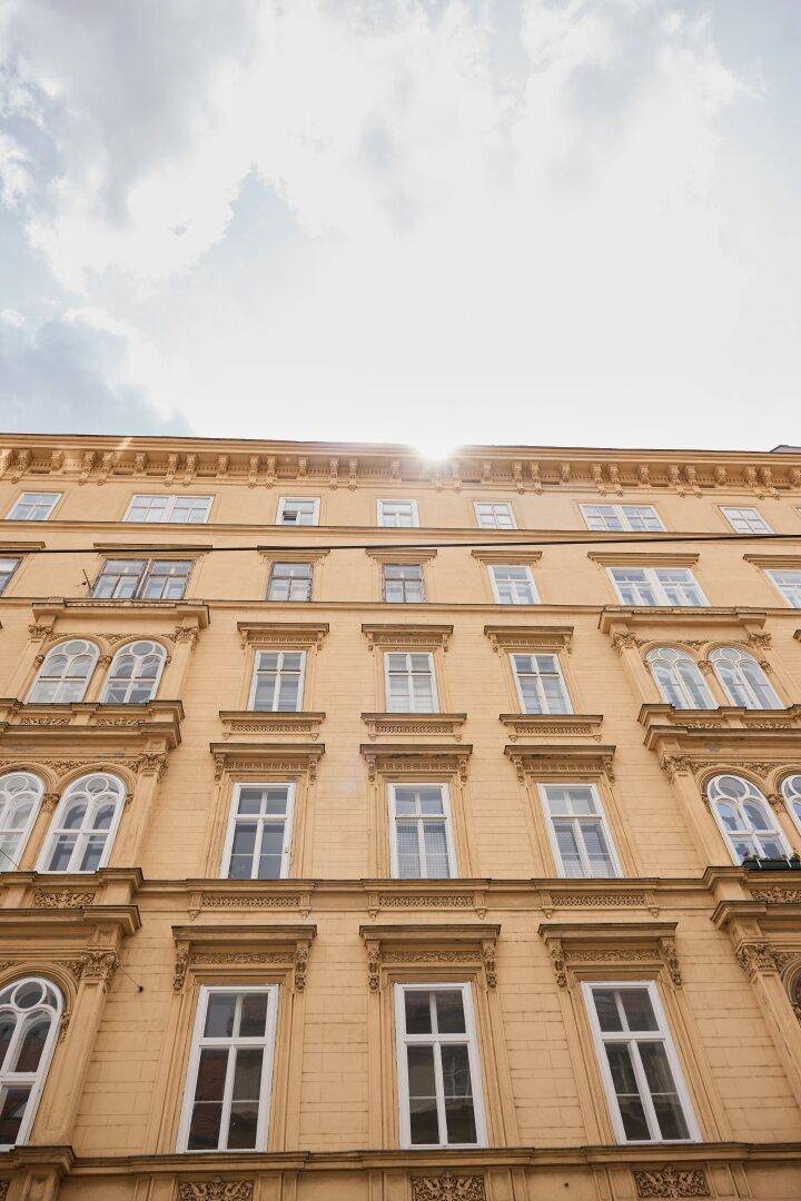 Historische Gebäudefassade mit vielen Fenstern und dekorativen Elementen im Sonnenlicht.
