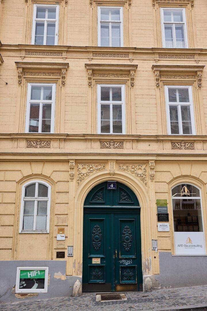 Historische Fassade eines Gebäudes mit einer verzierten Eingangstür und klassischen Fenstern.