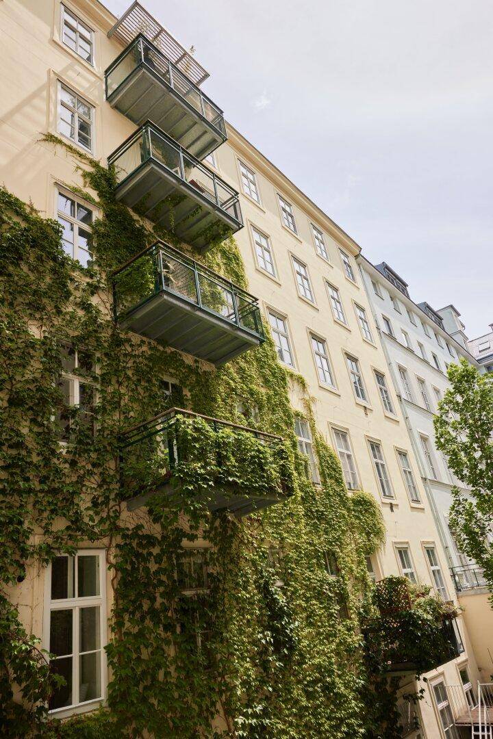 Fassade eines Altbaus, üppig mit Efeu bewachsen, mit mehreren kleinen Balkonen übereinander.