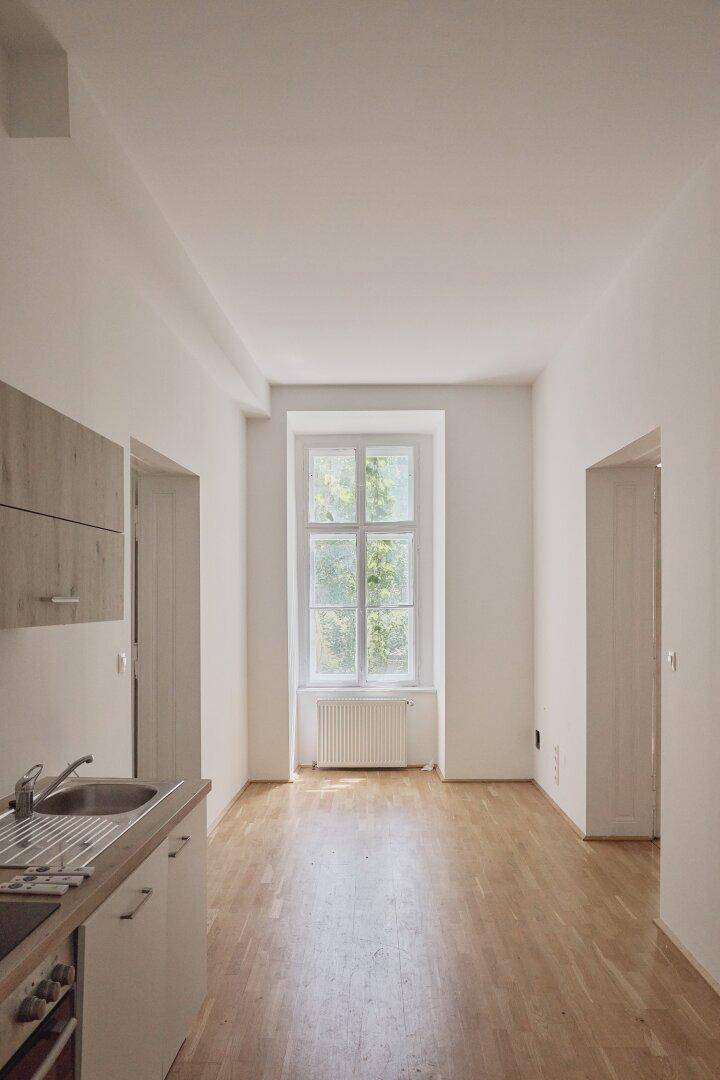 Helle Küche mit Holzdielenboden, Fenster und einer kompakten Küchenzeile mit Spüle und Oberschrank.
