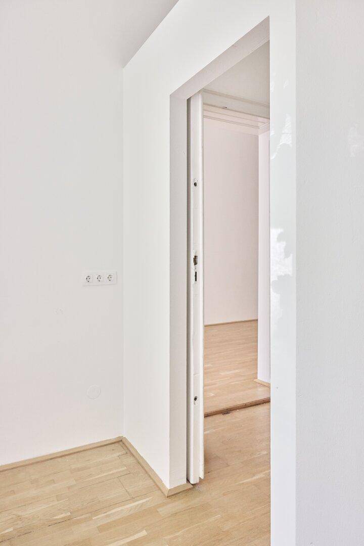 Heller Durchgang zu einem weiteren Raum mit Holzboden und weißen Wänden.