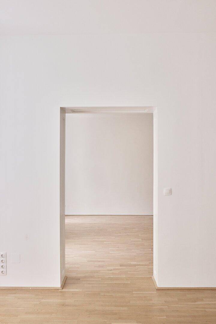 Offener Durchgang zwischen zwei hellen Räumen mit Holzboden.
