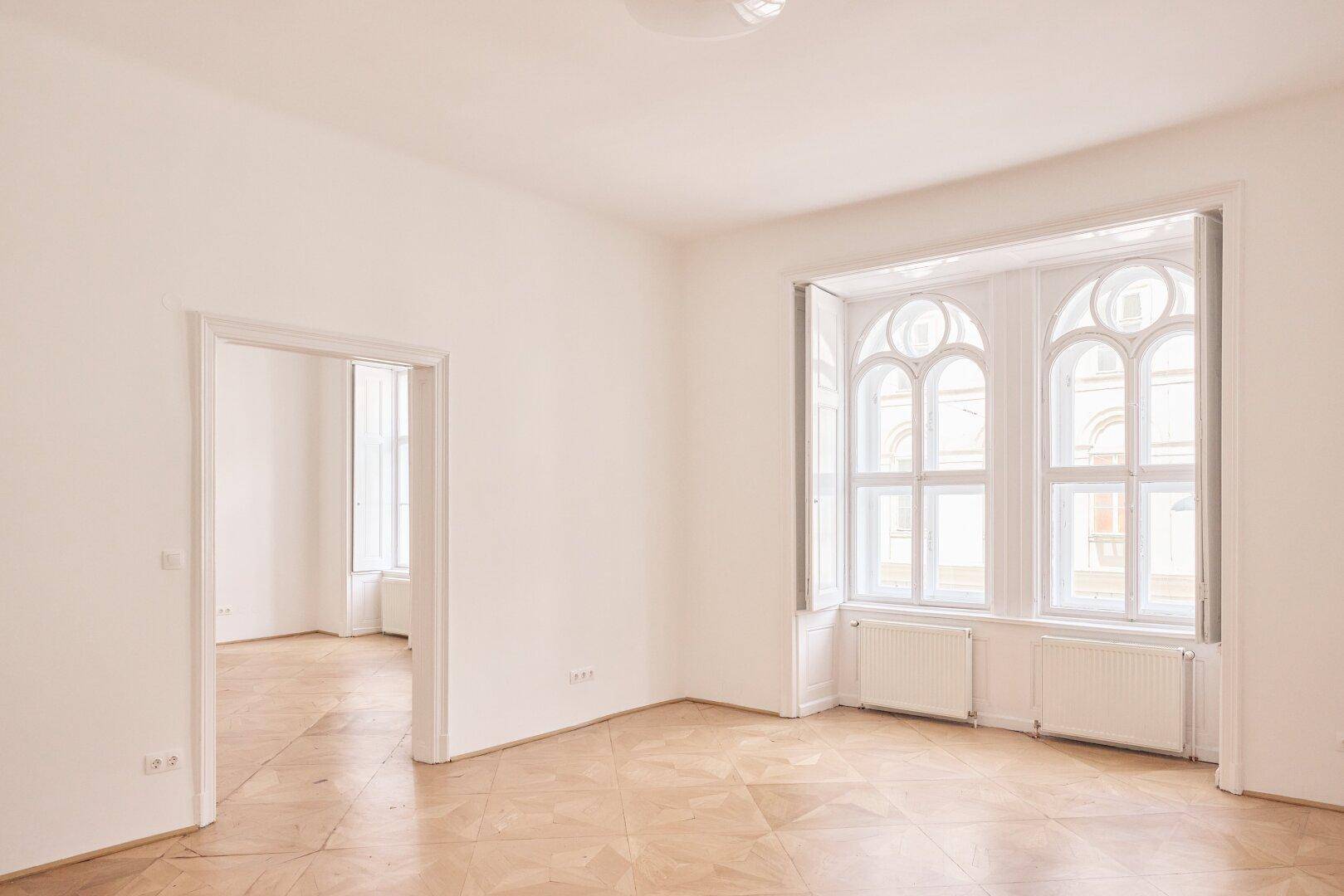 Heller Raum mit kunstvollen Fenstern, Parkettboden und Blick nach draußen.