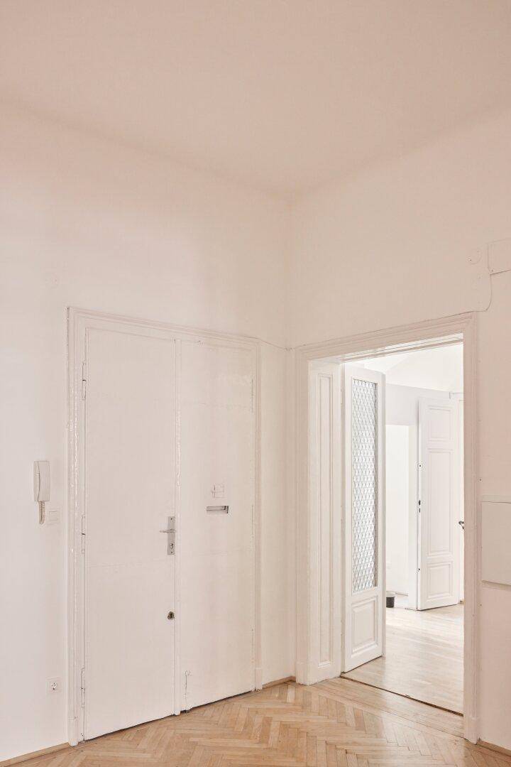 Heller Flur mit Eingangstür und einer weiteren Tür, die zu einem Zimmer führt.