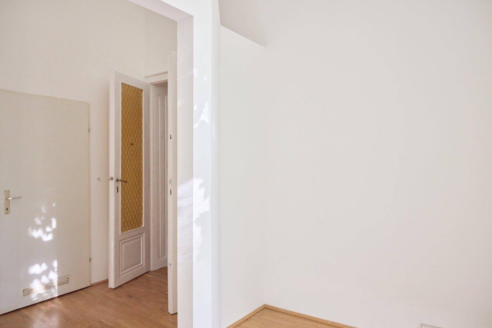 Heller Eckbereich mit Holzboden und einer Tür, die zu einem weiteren Raum führt.