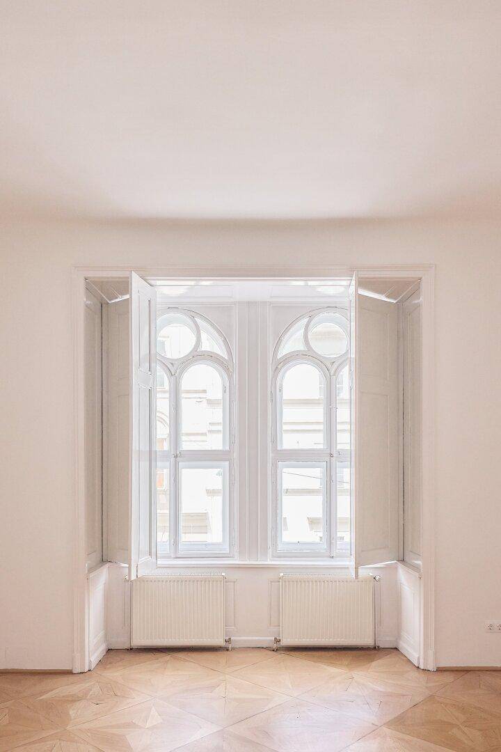 Detailansicht der kunstvollen Fenster in einem hellen Raum mit Parkettboden.