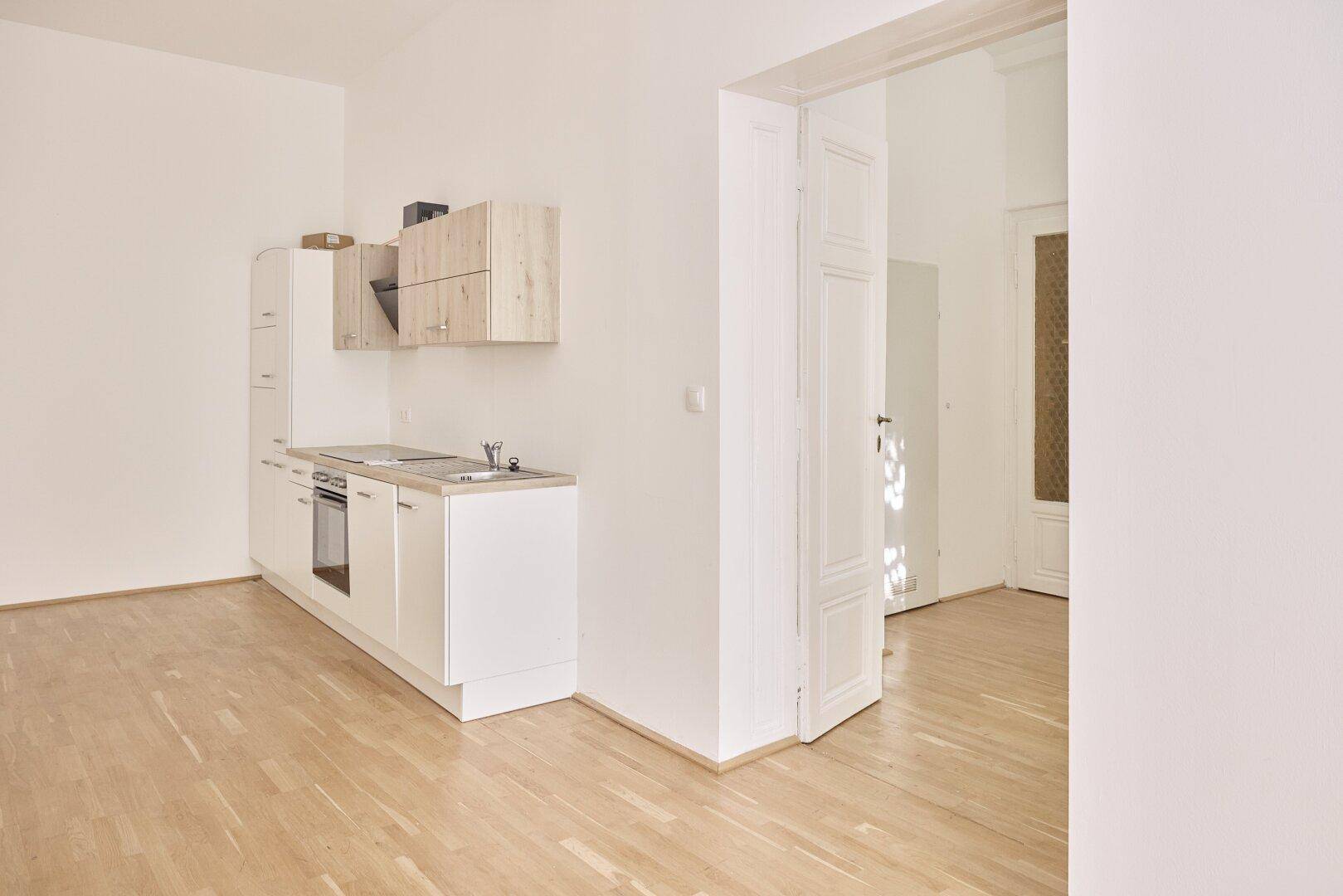 Heller Raum mit kleiner Küchenzeile und offenem Zugang zu einem weiteren Zimmer.