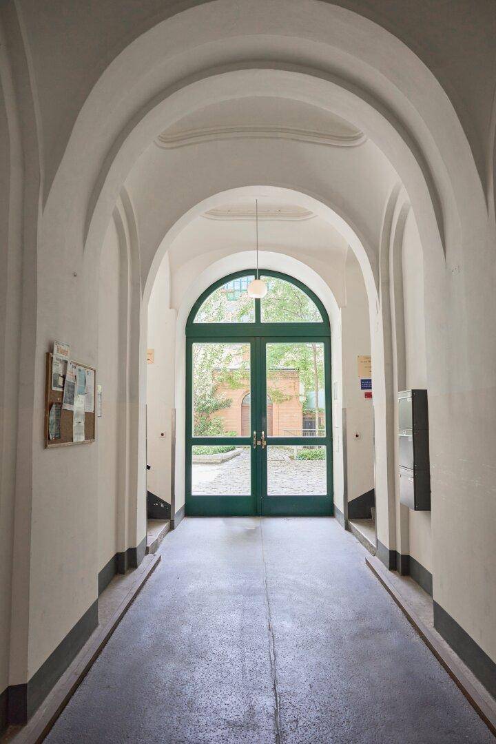 Langer, gewölbter Flur im Erdgeschoss eines Altbaus mit grüner Glastür zum Innenhof.