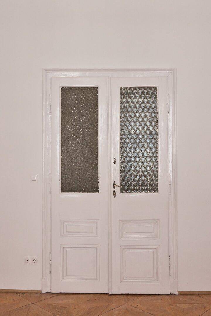 Geschlossene Doppeltür mit strukturierten Glaseinsätzen und traditionellen Beschlägen in einem hellen Raum.
