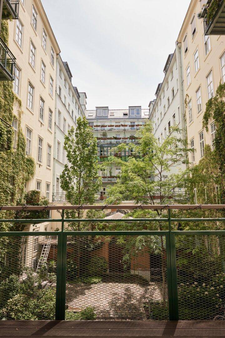 Blick von einem Balkon in einen grünen Innenhof mit Bäumen und Gebäuden.