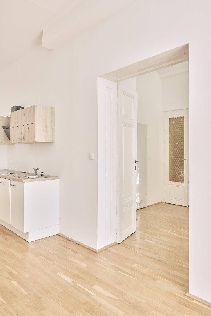 Heller Raum mit kleiner Küchenzeile und offenem Zugang zu einem weiteren Zimmer.