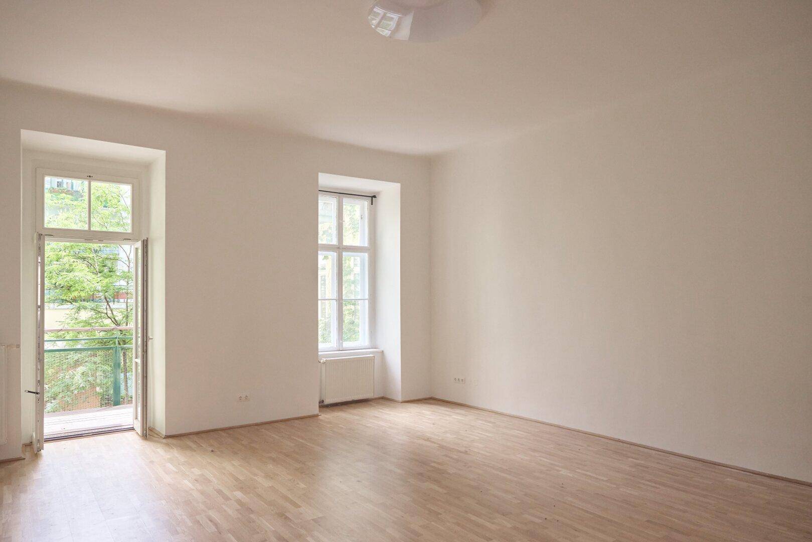 Heller Raum mit Zugang zu einem Balkon und einem weiteren Fenster, bietet viel Licht.