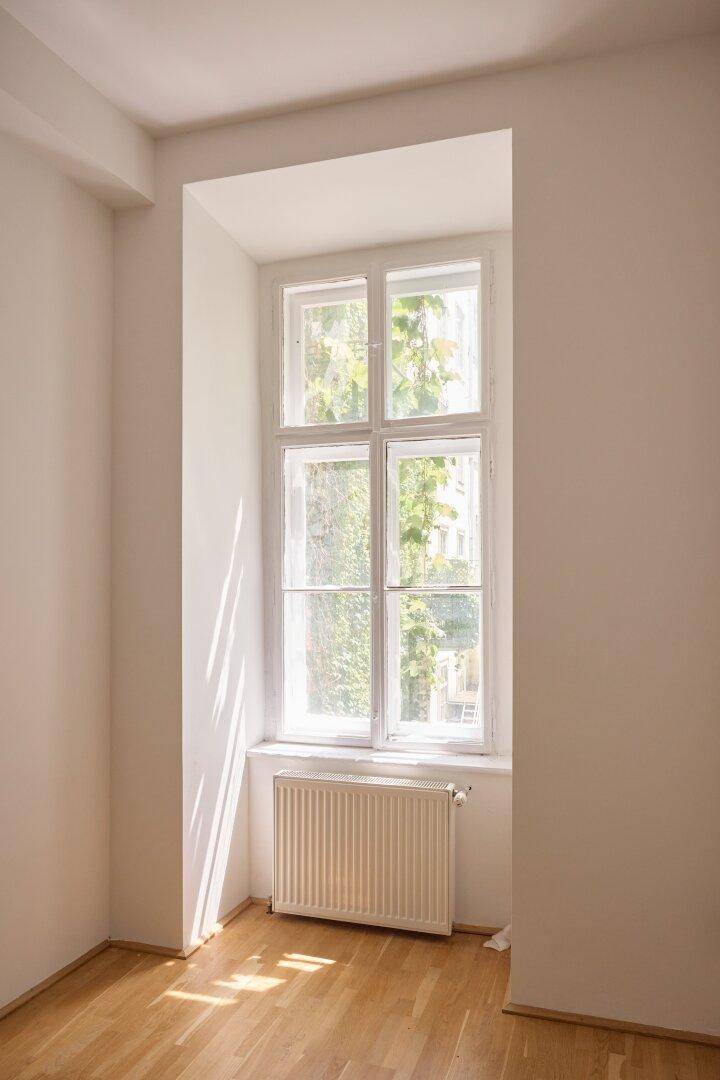 Heller Raum mit einem Fenster, durch das Sonnenlicht einfällt, und Holzboden.