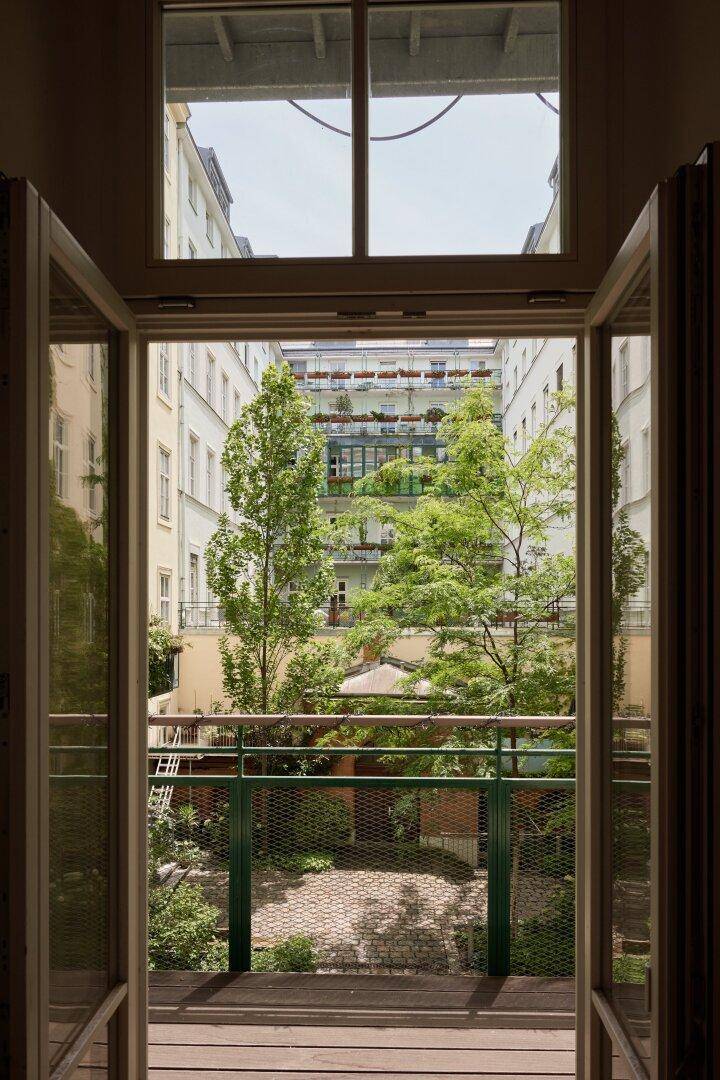 Blick aus einem Fenster auf einen Balkon und den grünen Innenhof.