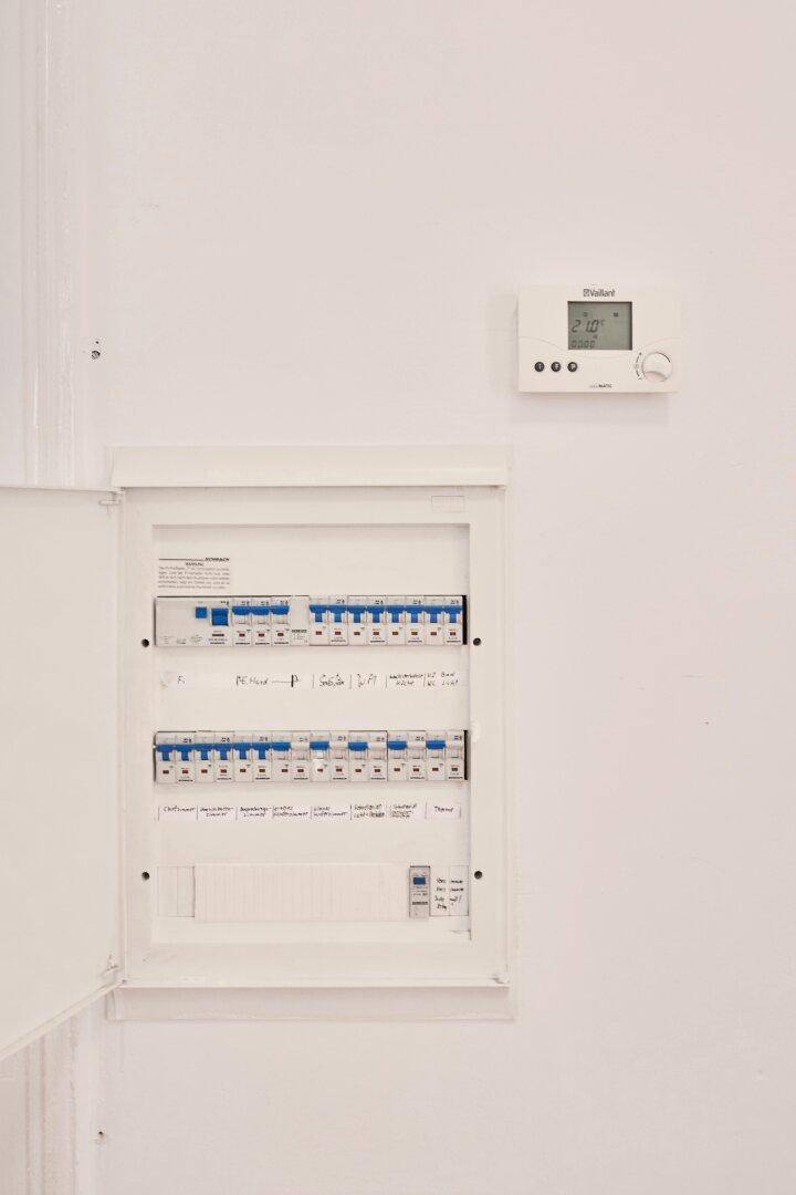 Sicherungskasten und digitaler Thermostat an einer weißen Wand in einem Hauswirtschaftsraum.