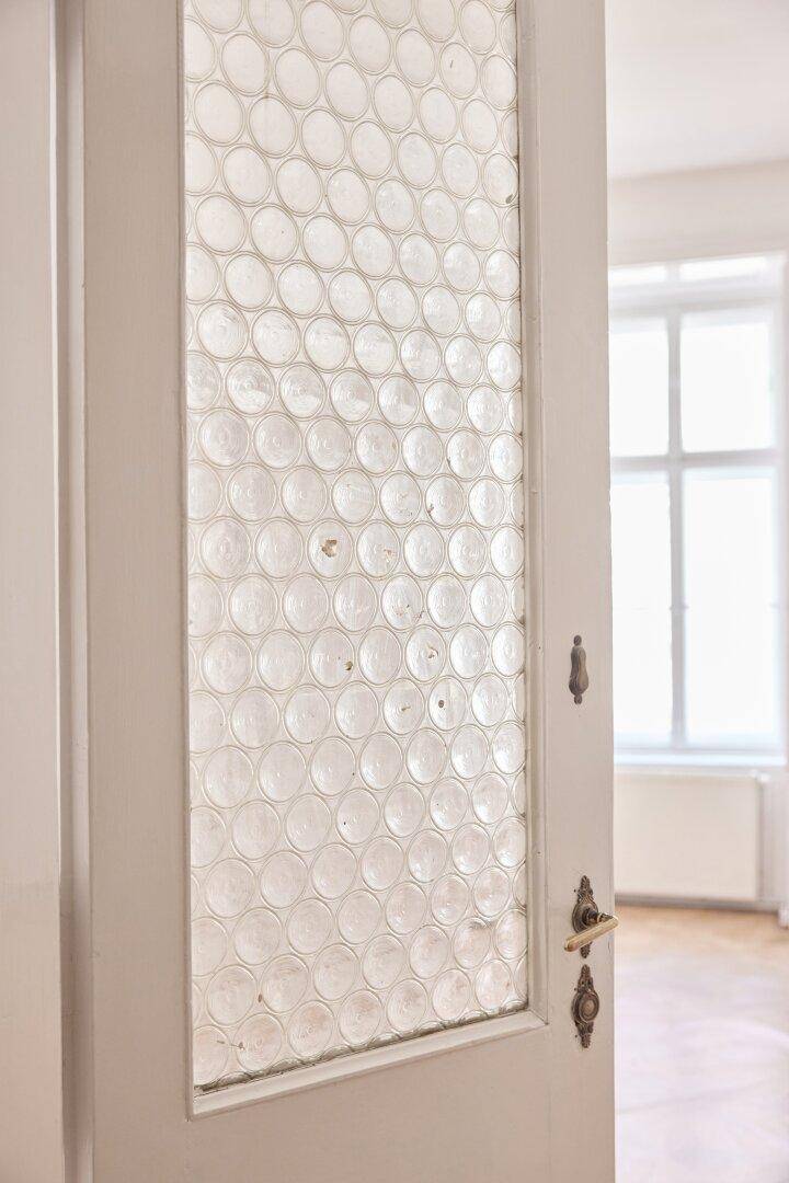 Detailansicht einer Tür mit gemustertem Glas, die zu einem hellen Raum führt.