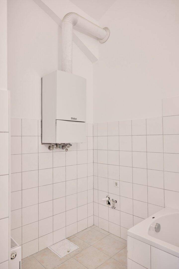 Gastherme von Vaillant in einem gefliesten Raum, teilweise mit Badewanne sichtbar.