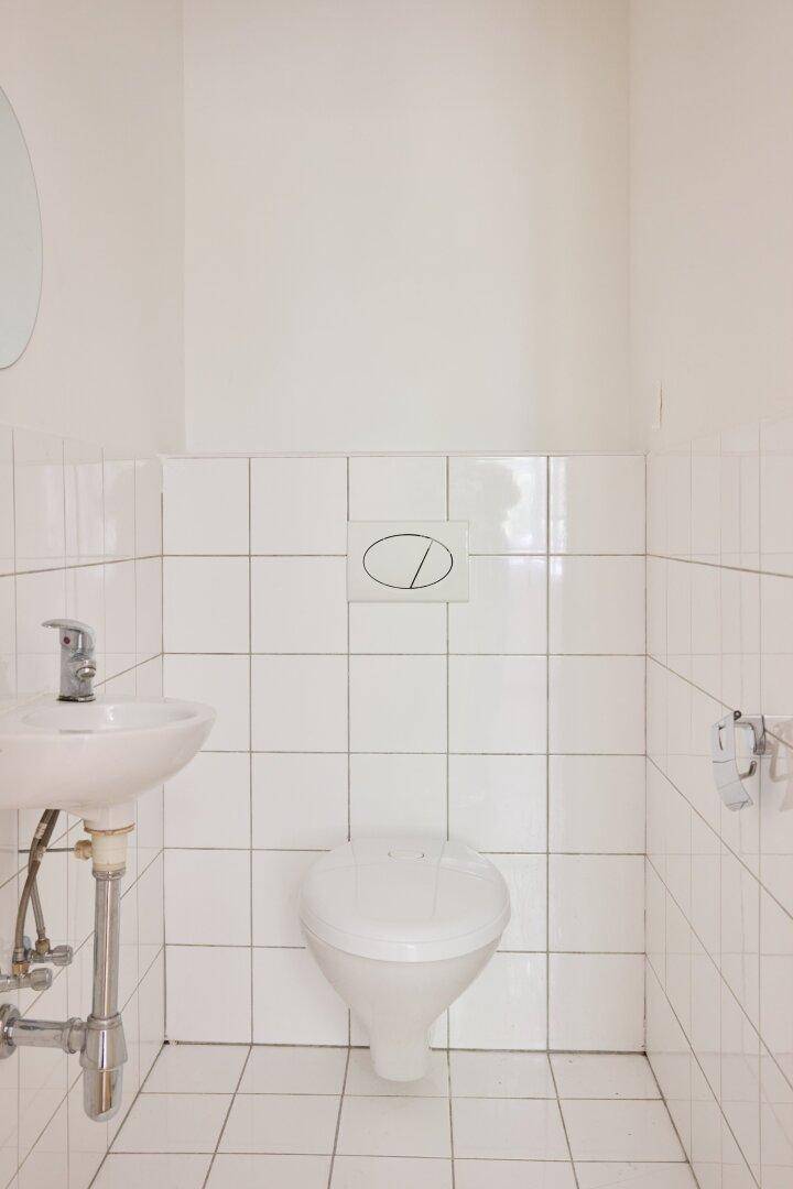 Kleines, hell gefliestes Gäste-WC mit Toilette, Waschbecken und rundem Spiegel.