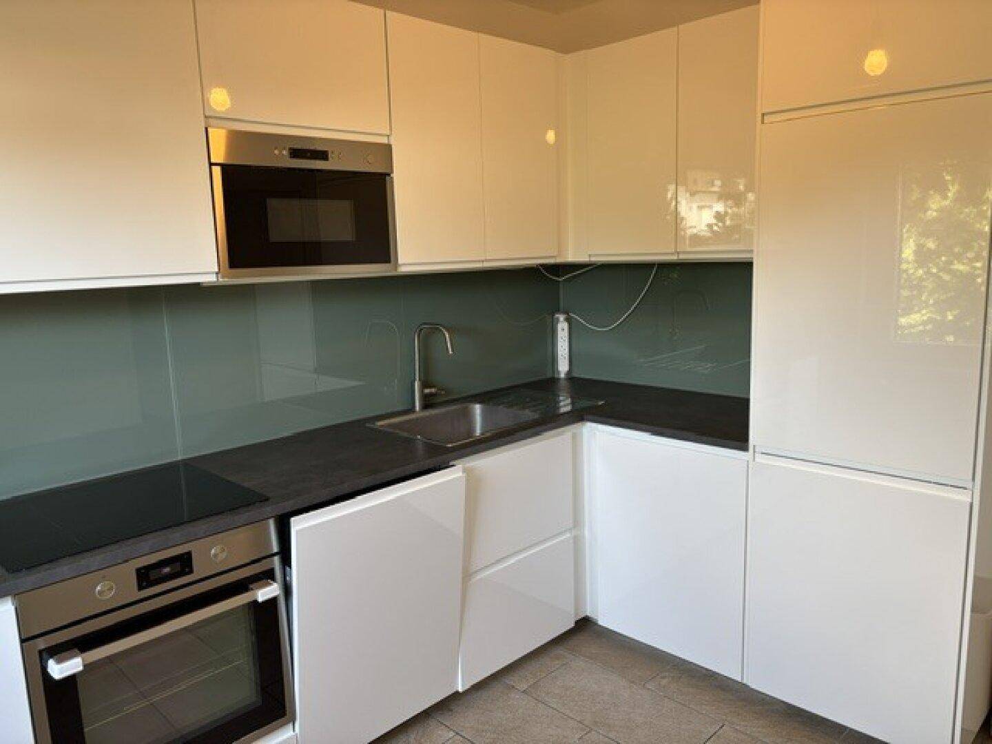 Moderne Küche mit weißen Hochglanzfronten, dunkler Arbeitsplatte und integrierten Geräten.