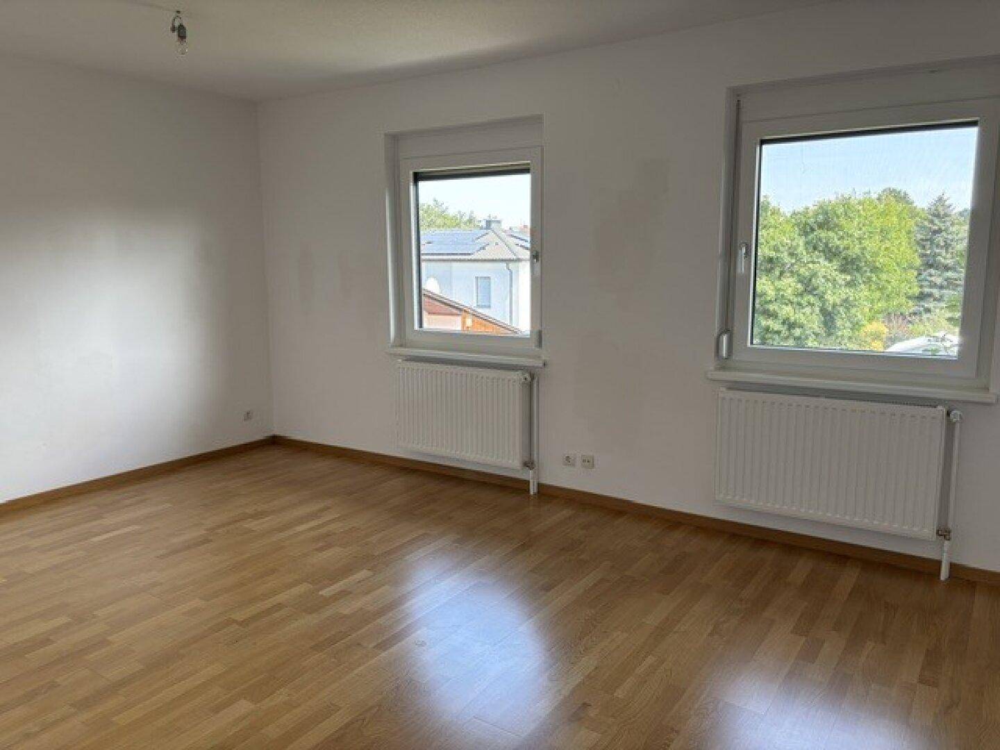 Heller Raum mit Parkettboden und zwei Fenstern, die viel Tageslicht hereinlassen.