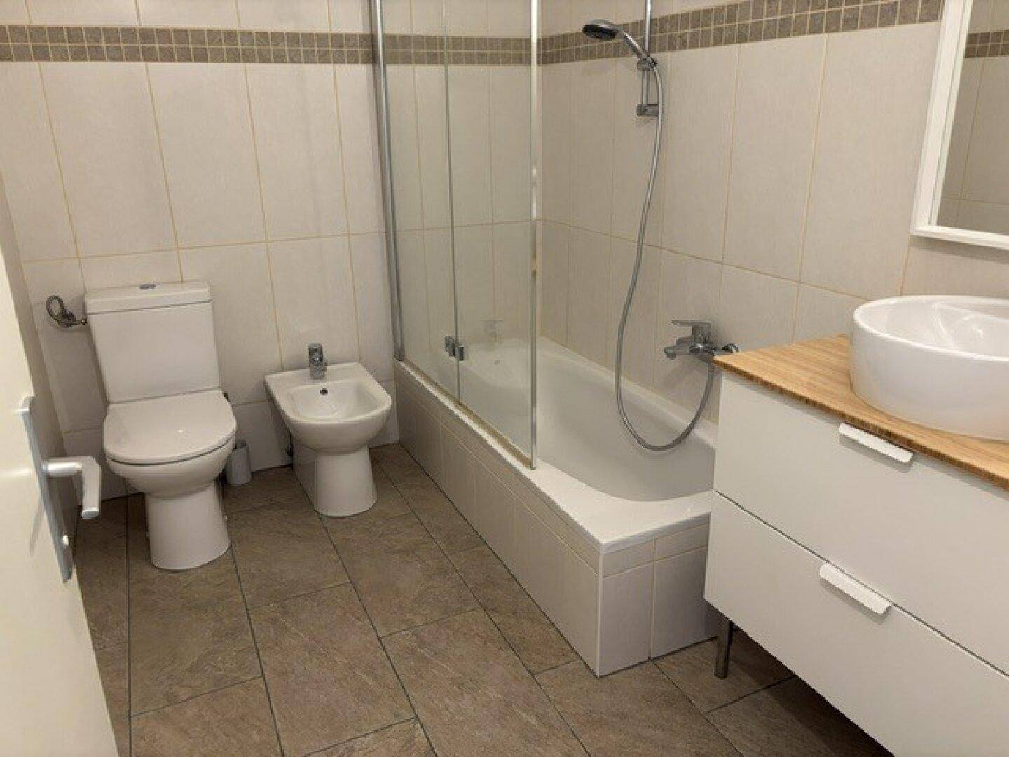 Gefliestes Badezimmer mit Badewanne, Duschabtrennung, WC, Bidet und Holzwaschtisch.
