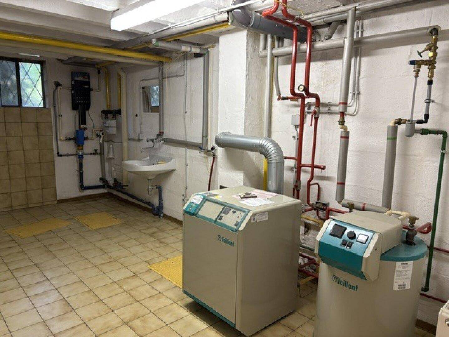 Technikraum im Keller mit Heizungsanlage, Rohren und Waschbecken.