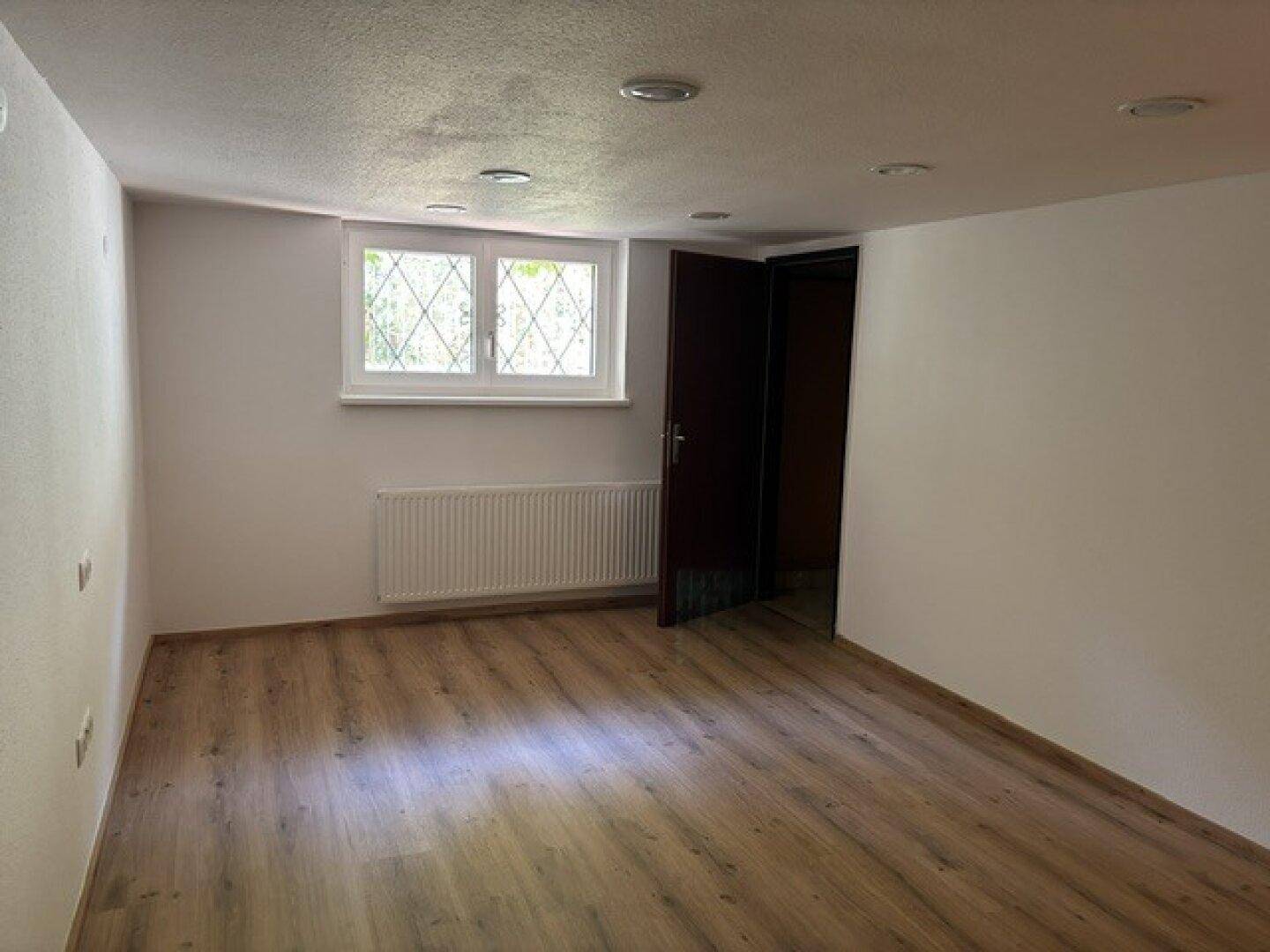 Heller Raum mit Laminatboden und Fenster, ausgestattet mit Deckenstrahlern.