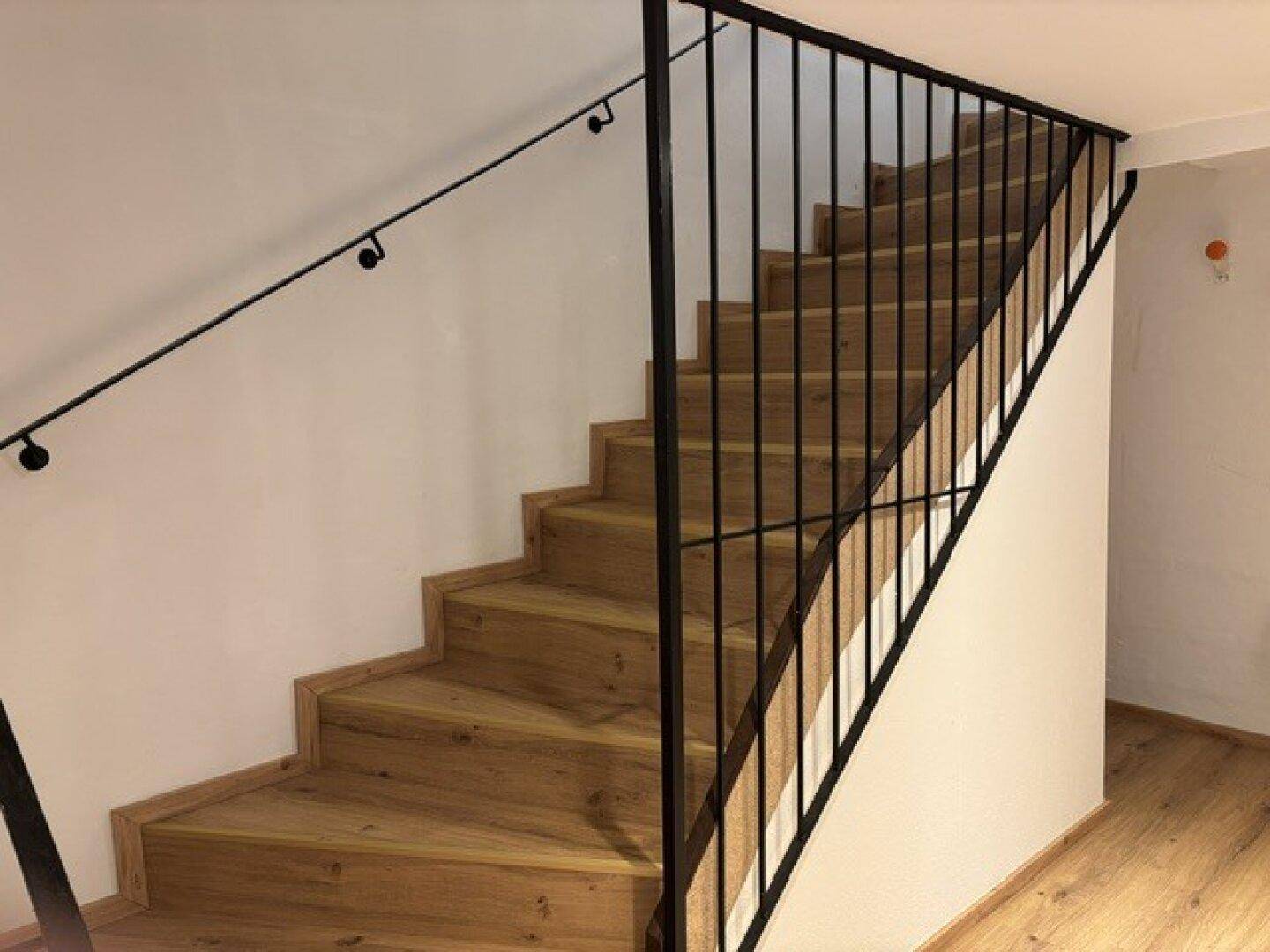 Moderne Holztreppe mit elegantem schwarzen Metallgeländer, die die Etagen verbindet.