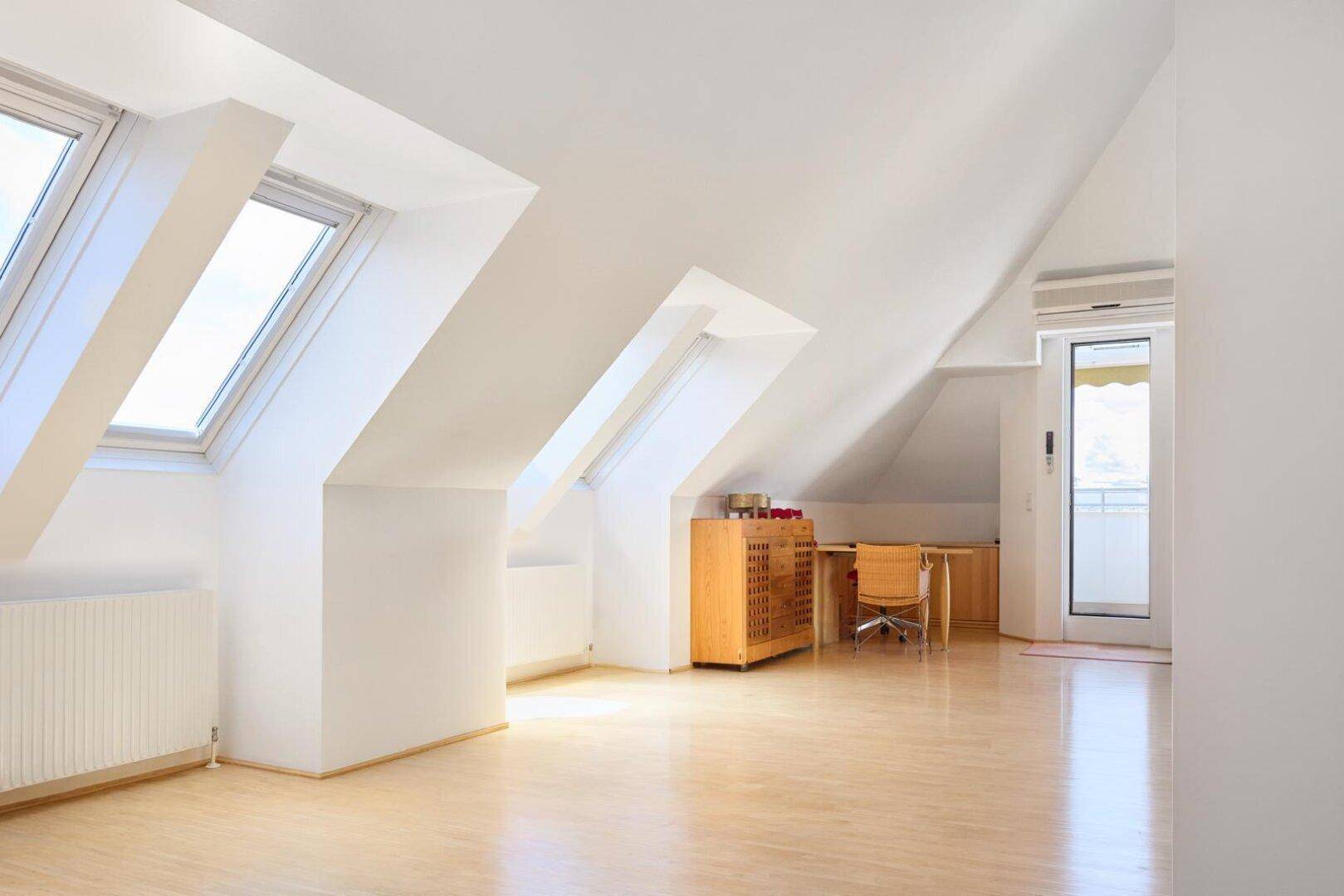 Lichtdurchfluteter Dachgeschossraum mit Holzboden, Dachfenstern und einem Arbeitsbereich.