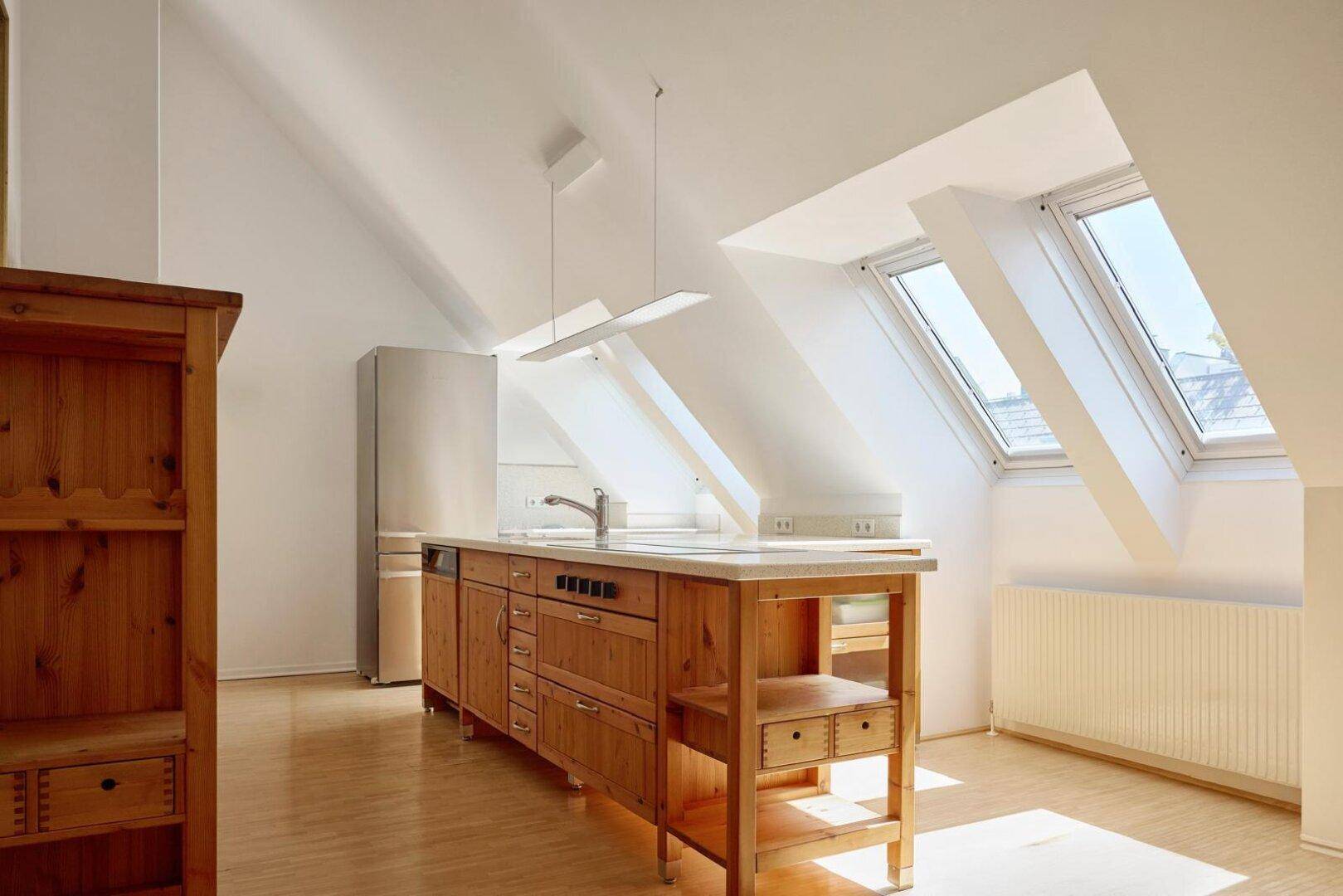 Helle Küche im Dachgeschoss mit Holzinsel, modernen Geräten und viel Tageslicht durch Dachfenster.