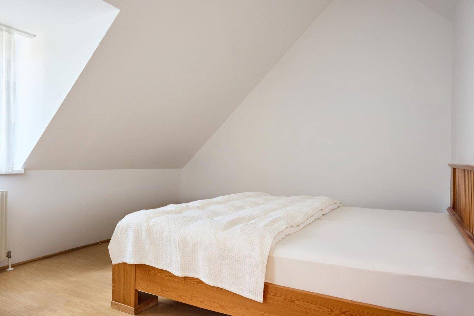 Gemütliches Schlafzimmer im Dachgeschoss mit Holzbett, schrägen Wänden und hellem Ambiente.