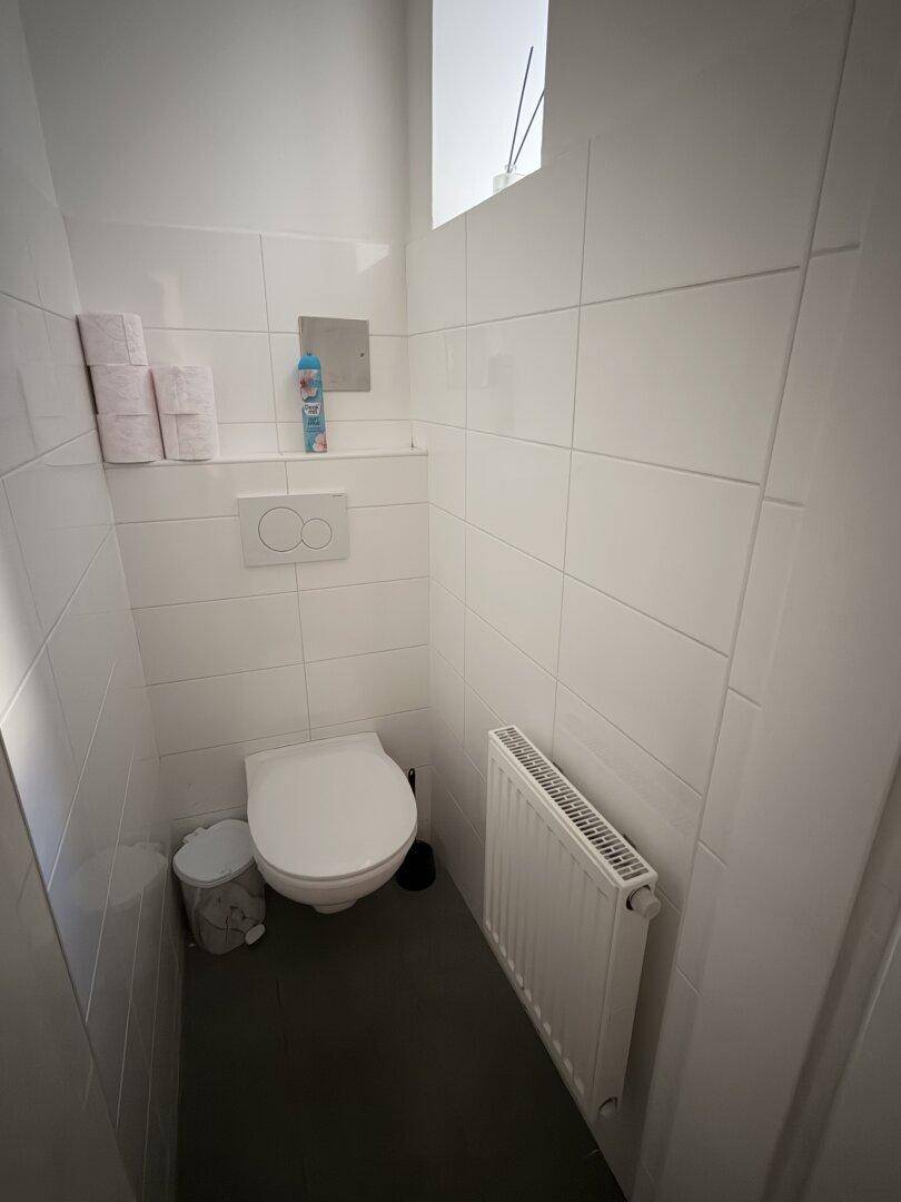 Kleiner Toilettenraum mit weißen Fliesen, wandhängendem WC und einem Heizkörper.