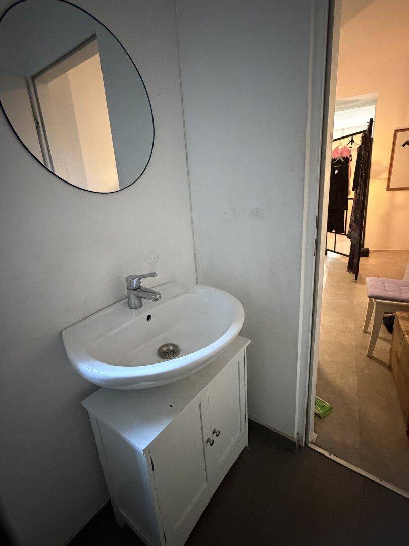 Waschbecken mit Unterschrank und rundem Spiegel in einem kleinen Toilettenbereich.