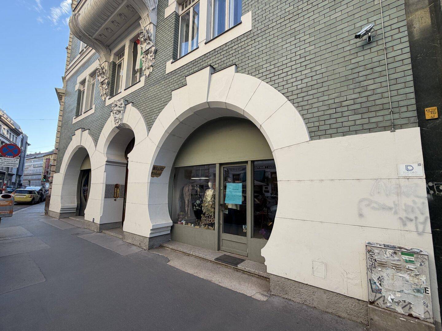 Gesamtansicht der Geschäftsfassade mit großen Rundbögen und einer Sicherheitskamera an der Seite.