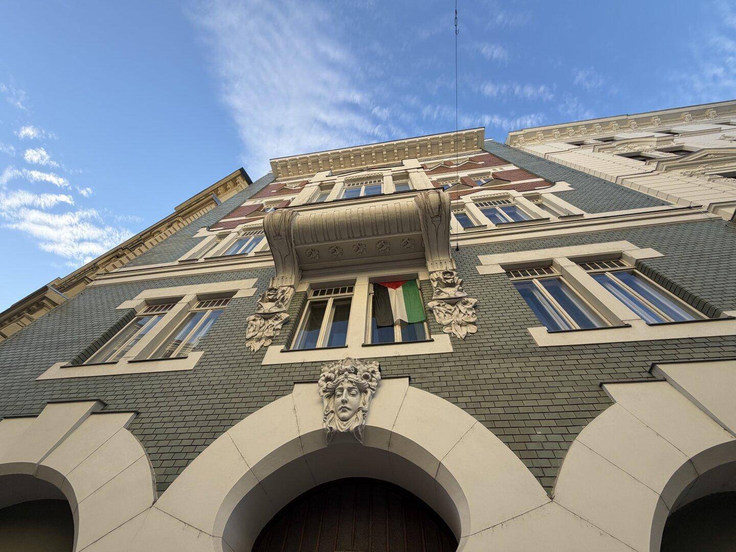 Detailaufnahme der historischen Fassade mit Balkon, kunstvollen Verzierungen und einem Fenster.