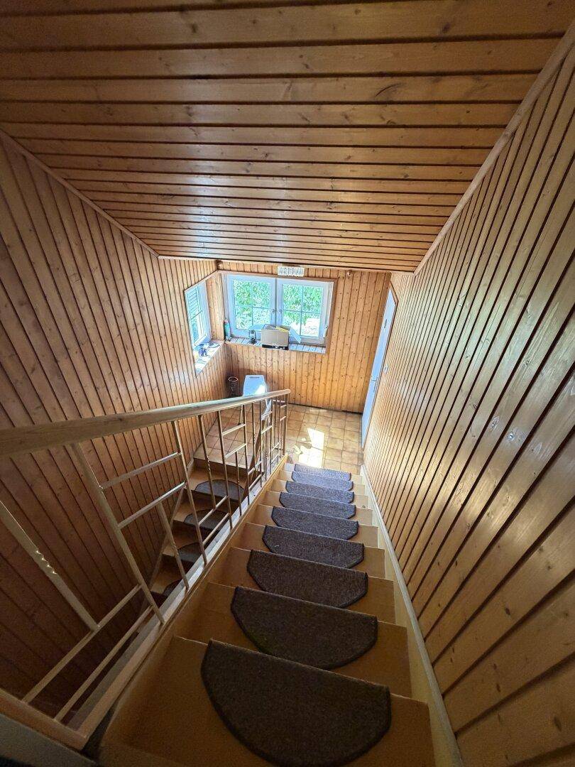 Holztreppe mit Teppichstufen und Holzverkleidung an Wänden und Decke, hell beleuchtet.